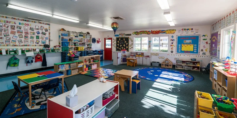An empty preschool classroom at Magic Hours in Mira Mesa, with a circle time rug, child-sized tables, book displays and learning centers